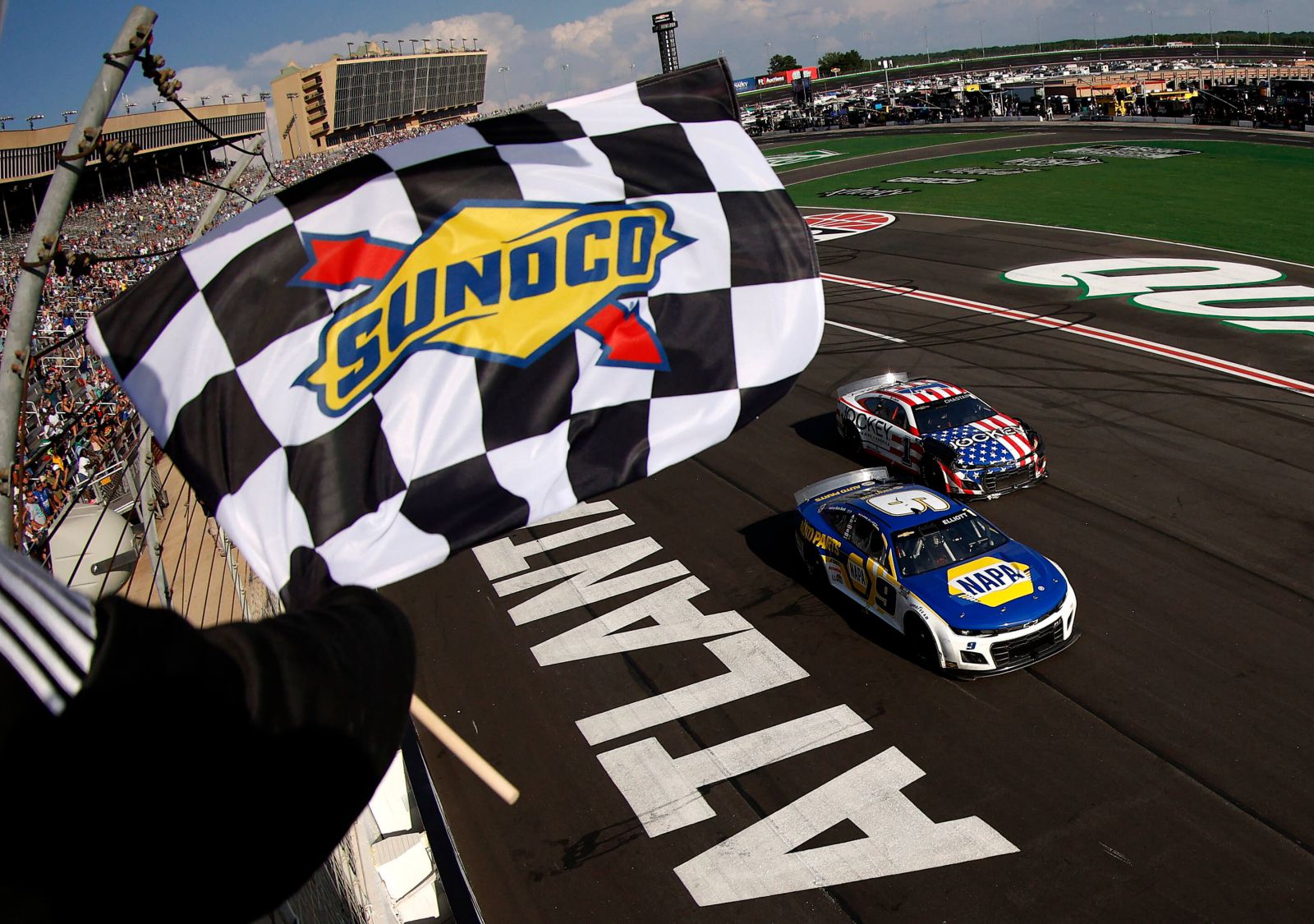 Race cars on track with Nascar official waving Sunoco checkered flag