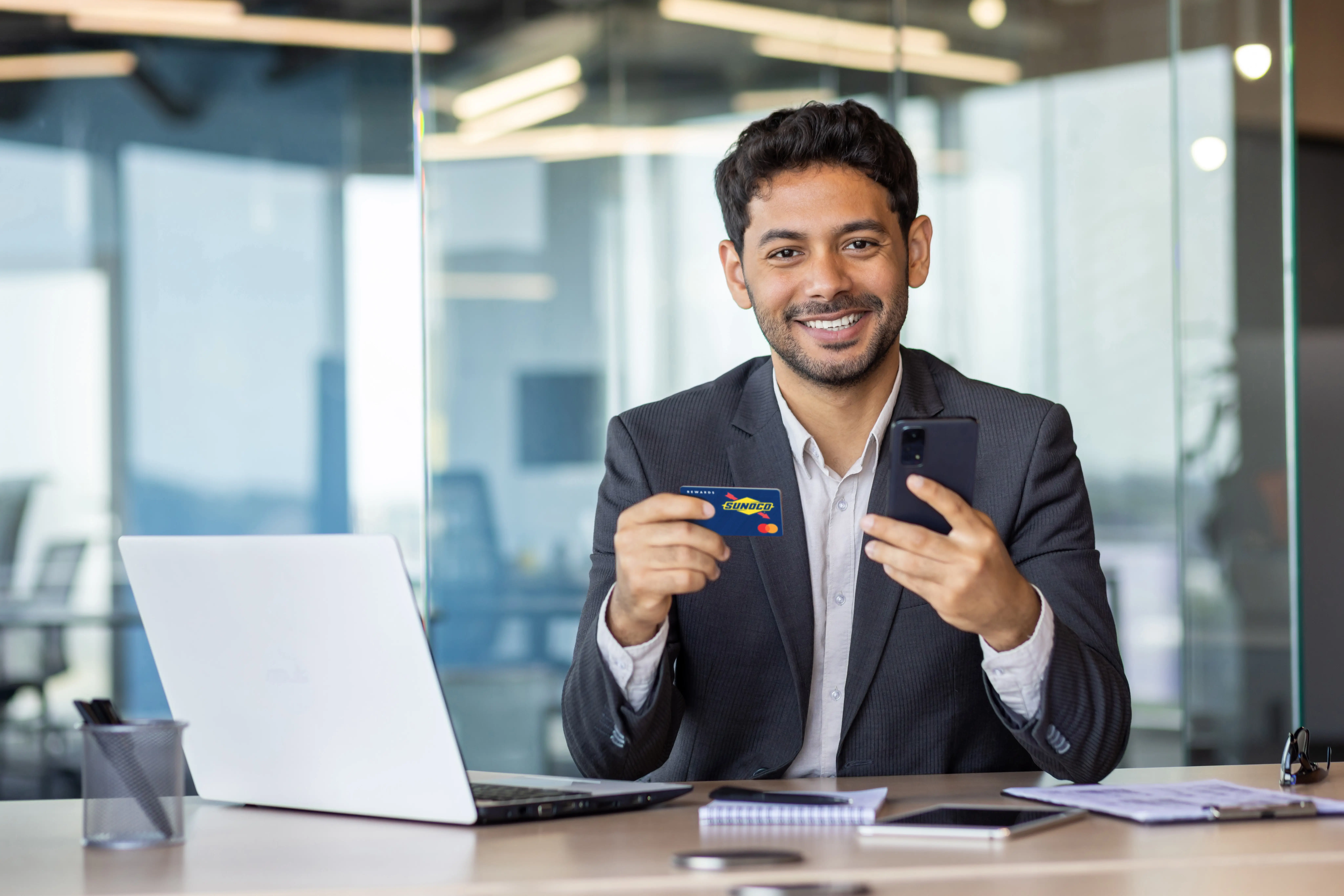 Man in office holding Sunoco credit card smiling at camera