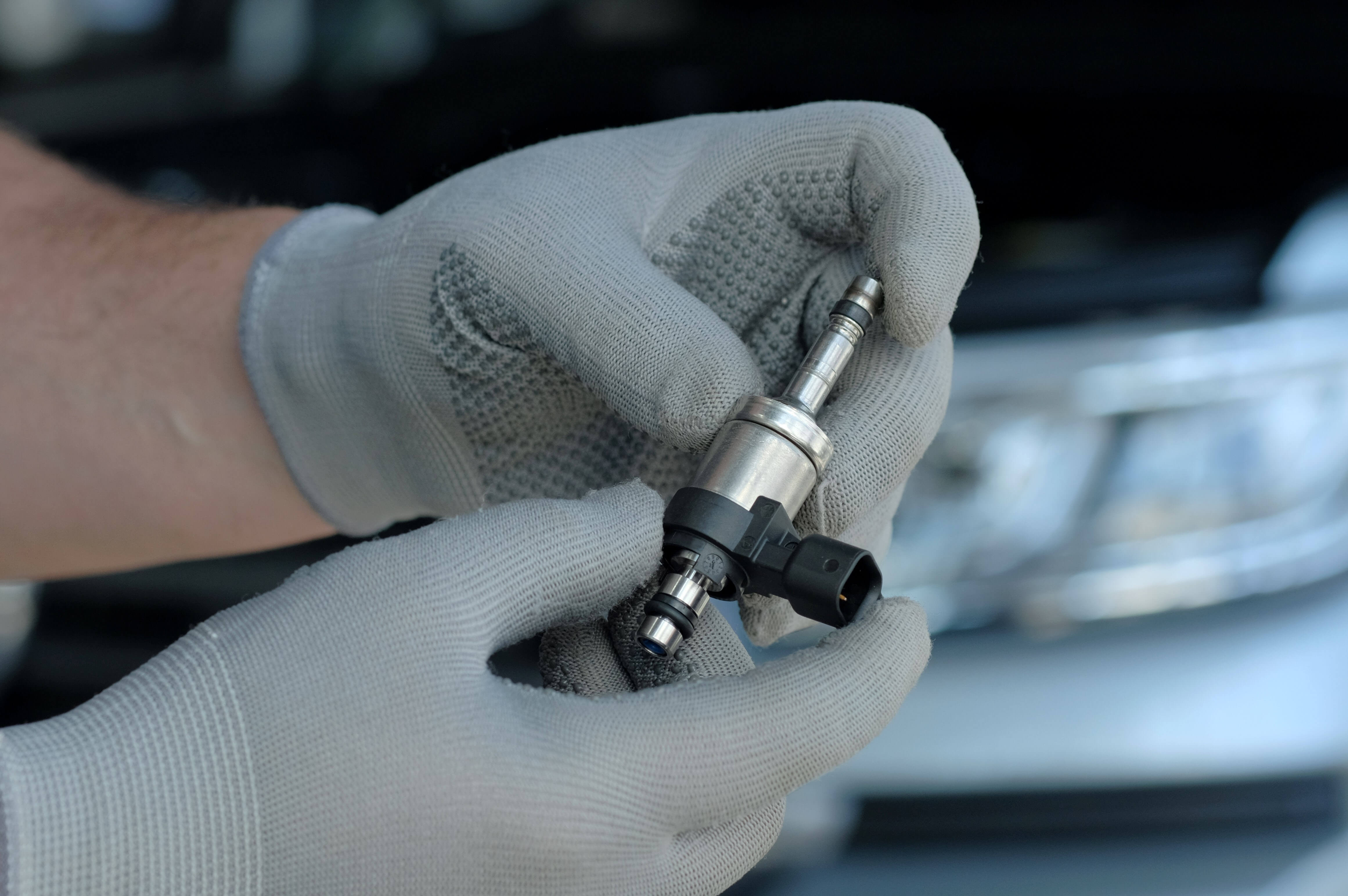 An auto mechanic holds a new fuel injector in his hands and checks the integrity of the spare part.