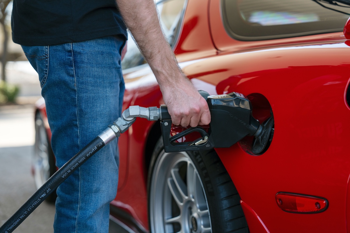 Man refueling red sports car with gas pump nozzle close-up
