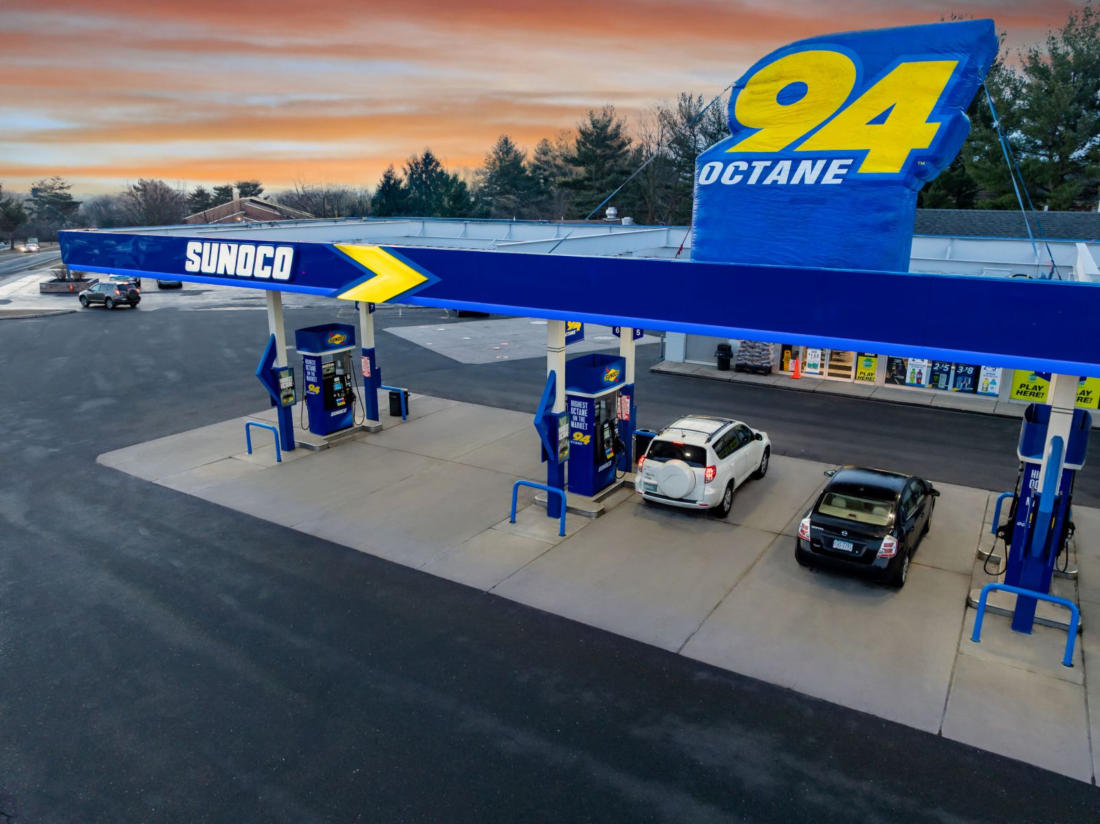 Sunoco gas station offering 94 Octane fuel at sunset, with cars fueling at premium gas pumps